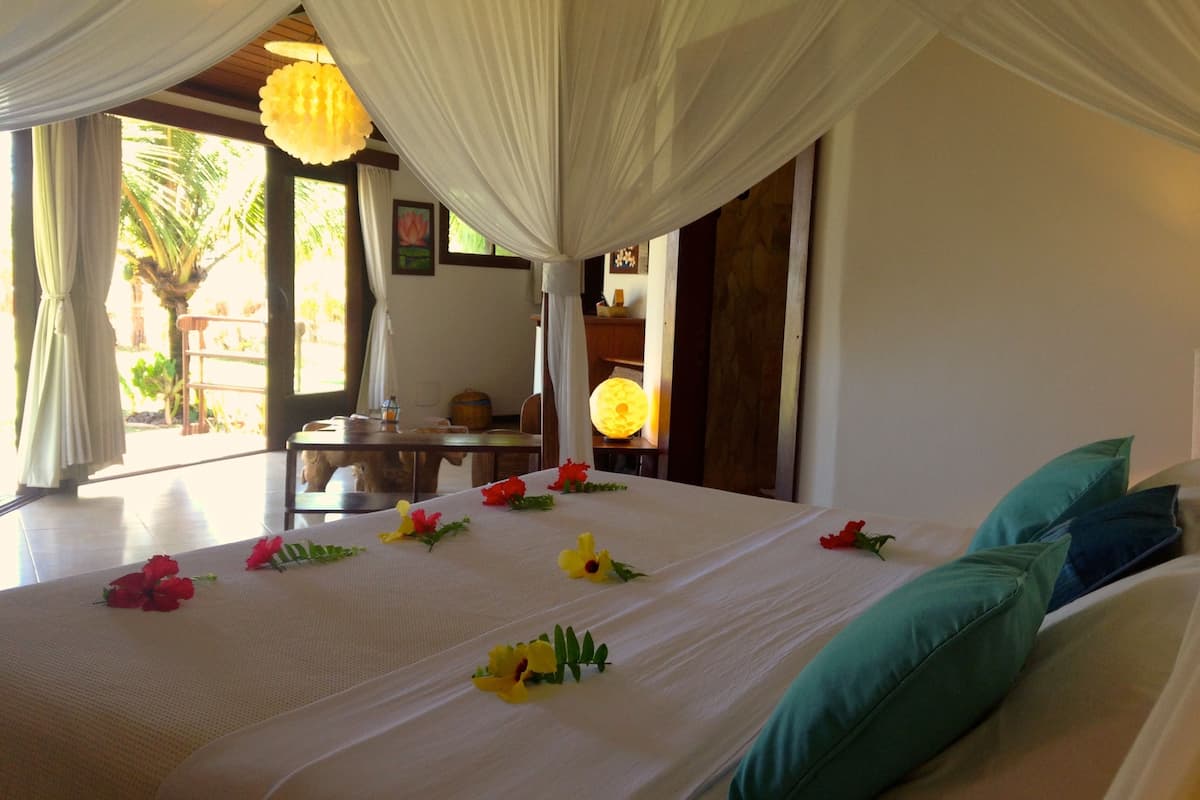 A bed with white linens and colorful flowers, teal pillows, and a canopy.