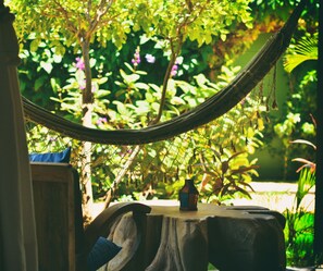 A hammock tied between two wooden posts with a small house model on a wooden table in the background.