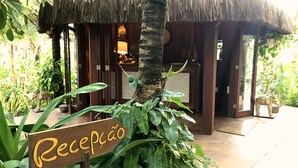 Un área de recepción con techo de paja, paredes de madera y un cartel que dice "Recepção".