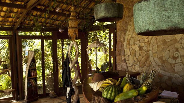 Un rústico espacio de bar con pared de piedra, techo de madera y un frutero en la barra.