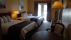 A hotel room with two beds, a desk, a chair, a lamp, and a large window with curtains. - Motel Cofotel (Saint-Simeon)
