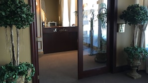 A reception area with a dark wooden reception desk labeled "Reception," a mirror reflecting the interior, and potted plants on either side. - Motel Cofotel (Saint-Simeon)
