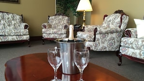 A room with floral-patterned armchairs, a wooden table with a champagne bucket and glasses, and a lamp. - Motel Cofotel (Saint-Simeon)