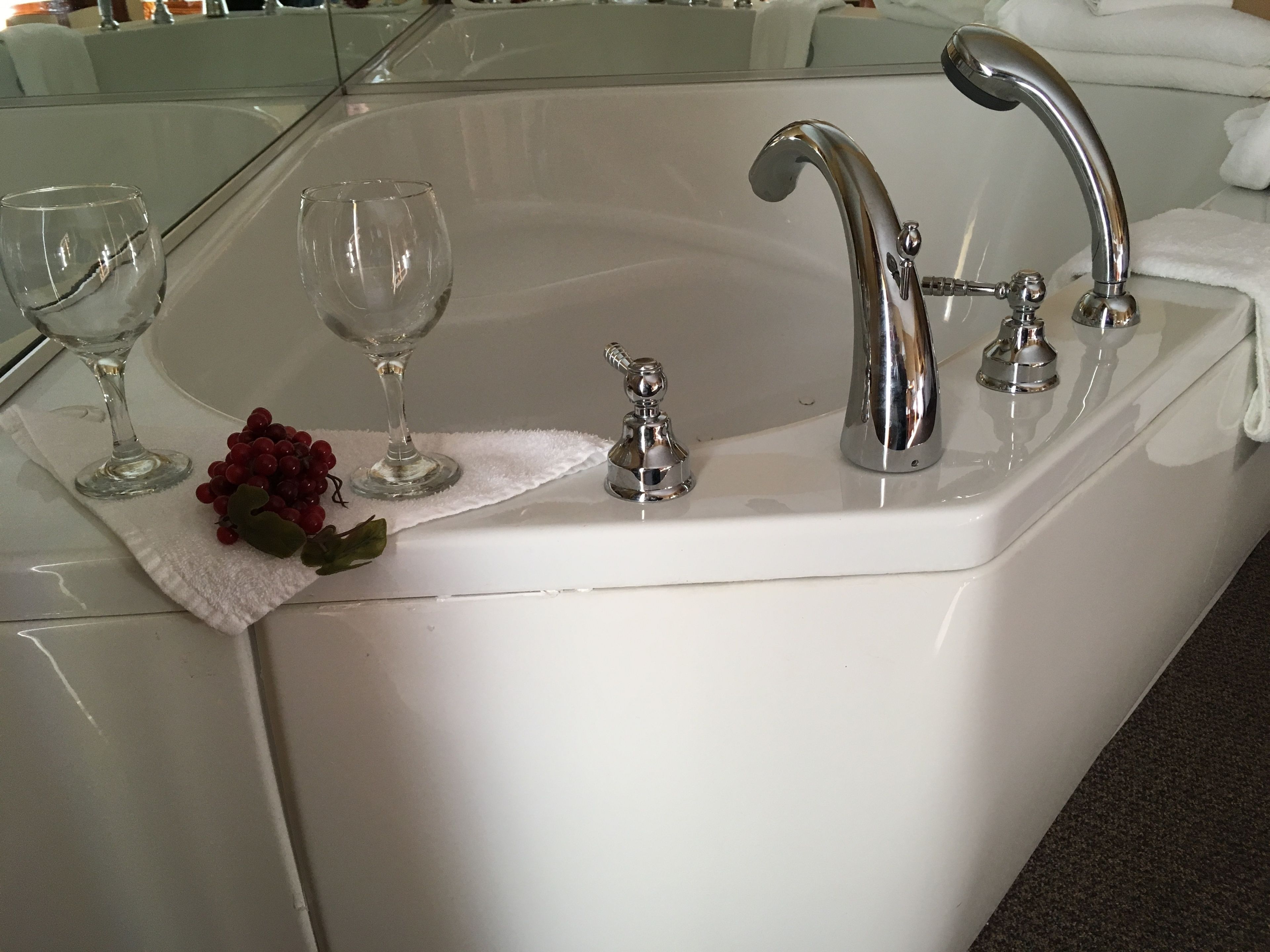 A bathroom with a white bathtub, two faucets, and two clear glass wine glasses on a white towel.