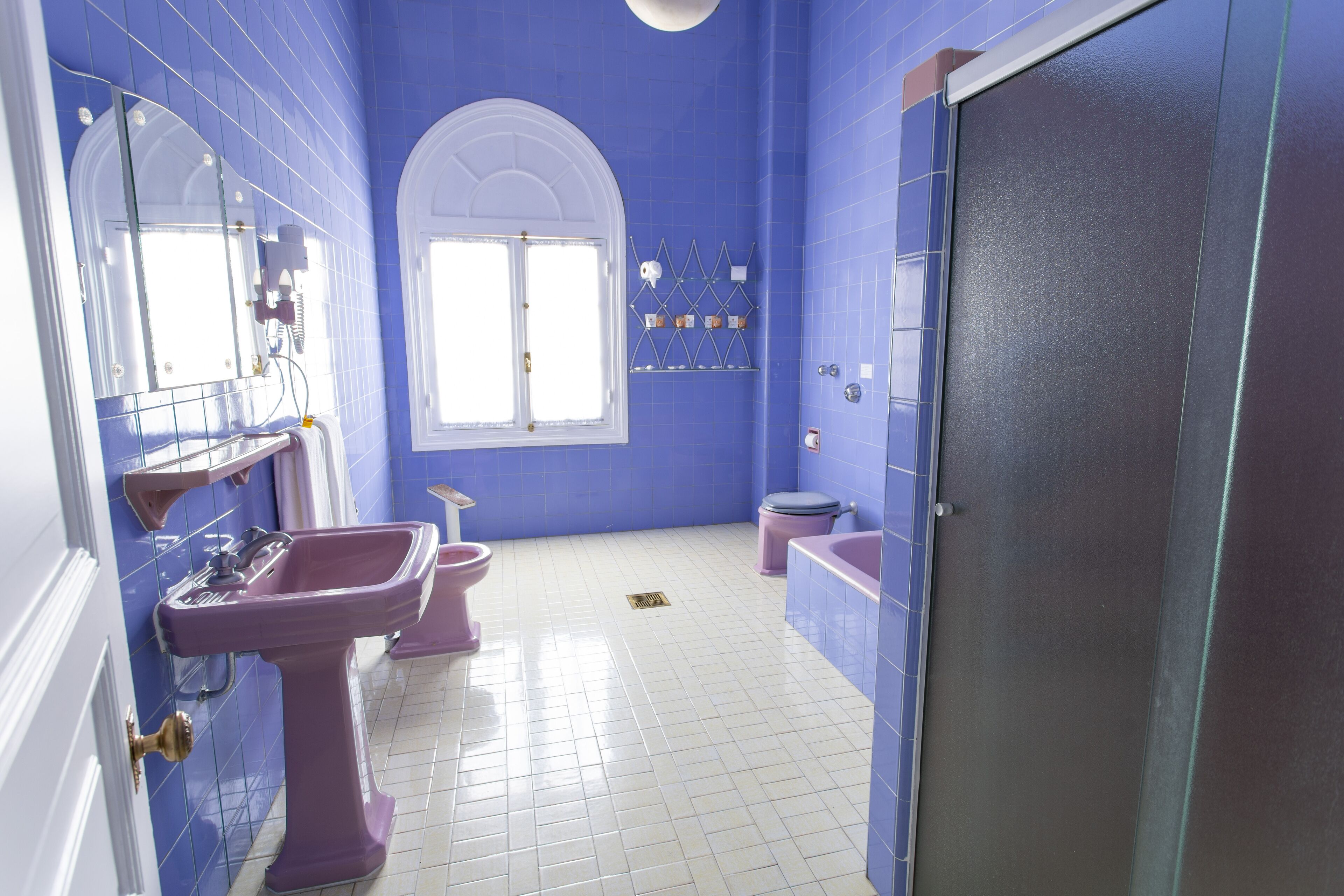 Un baño con paredes azules, azulejos blancos, un espejo grande, un lavamanos, un inodoro y una bañera.