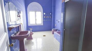 Un baño con paredes azules, azulejos blancos, un espejo grande, un lavamanos, un inodoro y una bañera.