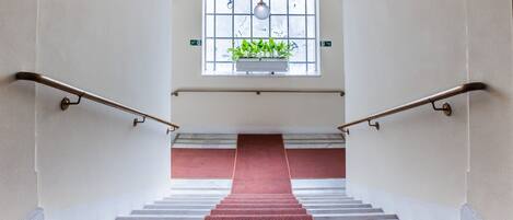 Una escalera con alfombra roja, barandales de metal y un ventanal con una planta.