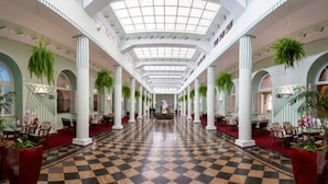 Un vestíbulo de hotel con piso a cuadros, columnas blancas y plantas verdes.