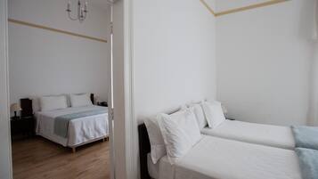 A hotel room with two single beds, a wooden floor, a white wall, and a door leading to another room.