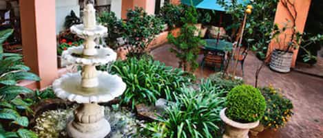 A garden with a tiered fountain, various potted plants, and outdoor furniture.