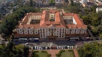 Vista aérea de um edifício grande e histórico, com um pátio central e vegetação ao redor.