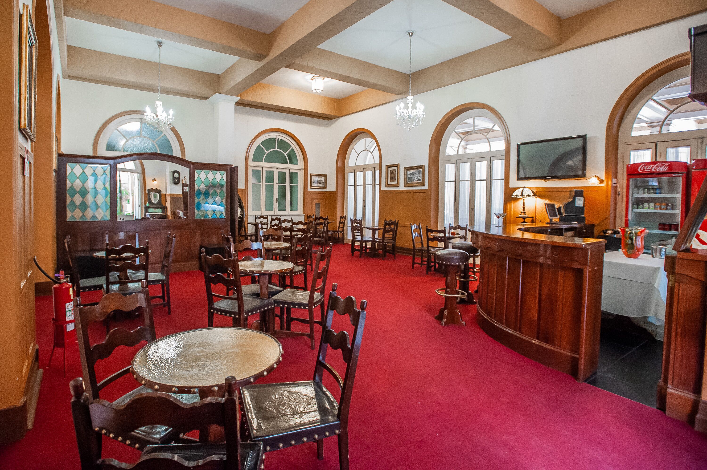 A hotel lobby with wooden furniture, a red carpet, arched windows, and a Coca-Cola refrigerator.