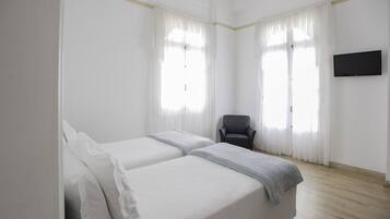 A hotel room with two beds, a chair, and a TV on the wall.