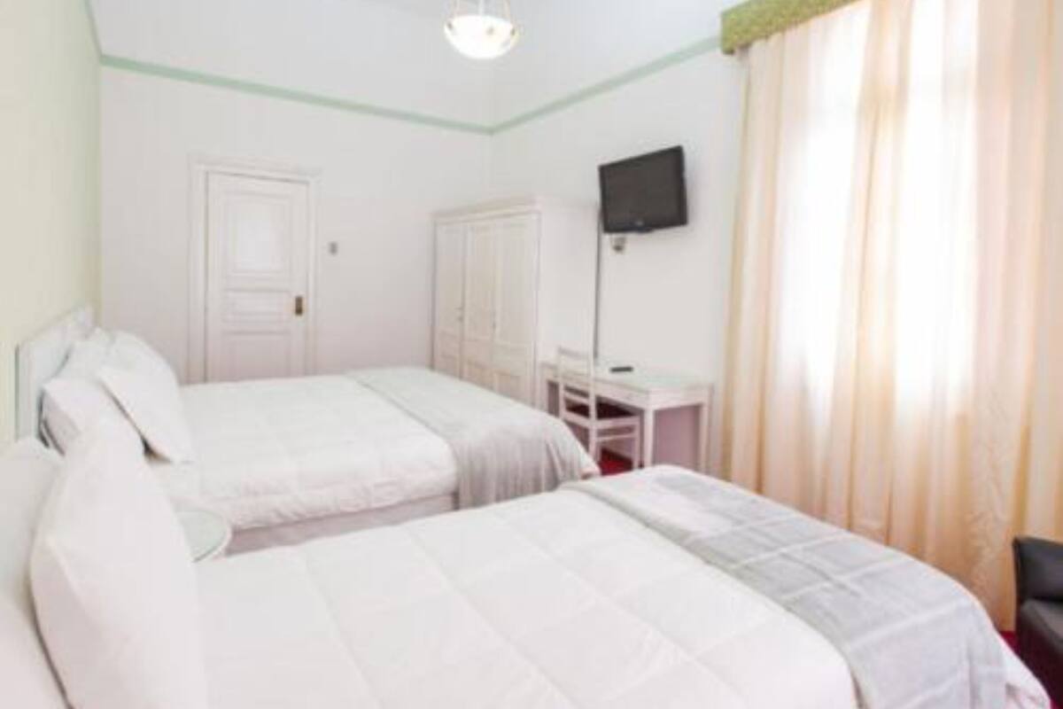Ein Zimmer mit zwei Betten, einem Schreibtisch, einem Stuhl, einem Fernseher und einem Fenster mit Vorhängen.