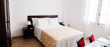Habitación de hotel ordenada con cama, mesita de noche, lámpara y una pequeña mesa con sillas.