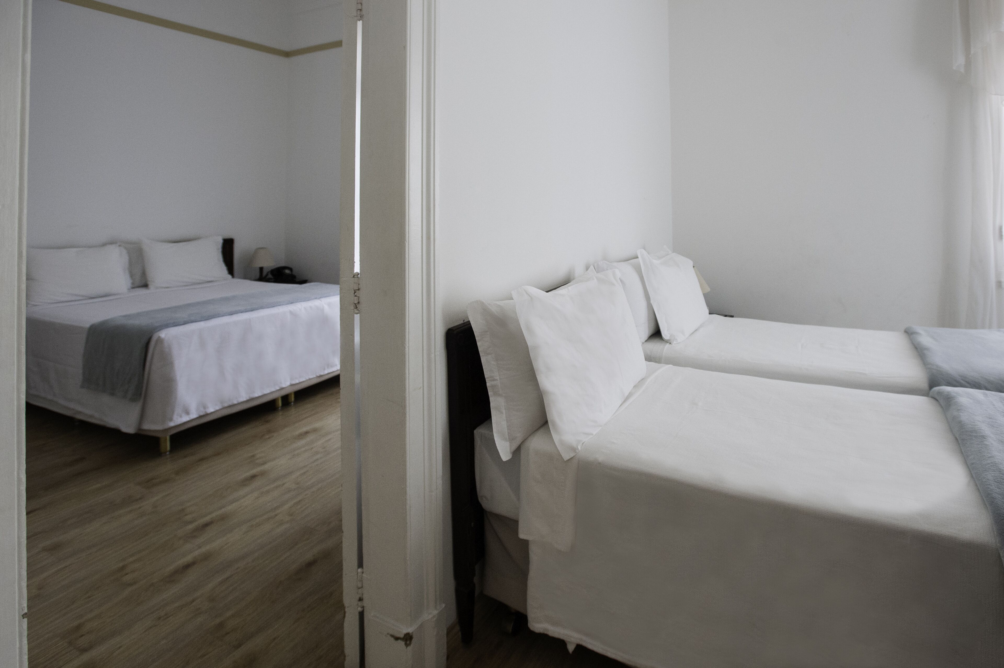 A room with two beds, a wooden floor, and white walls.