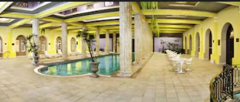 Un área de piscina con suelo de baldosas, columnas y arcos.
