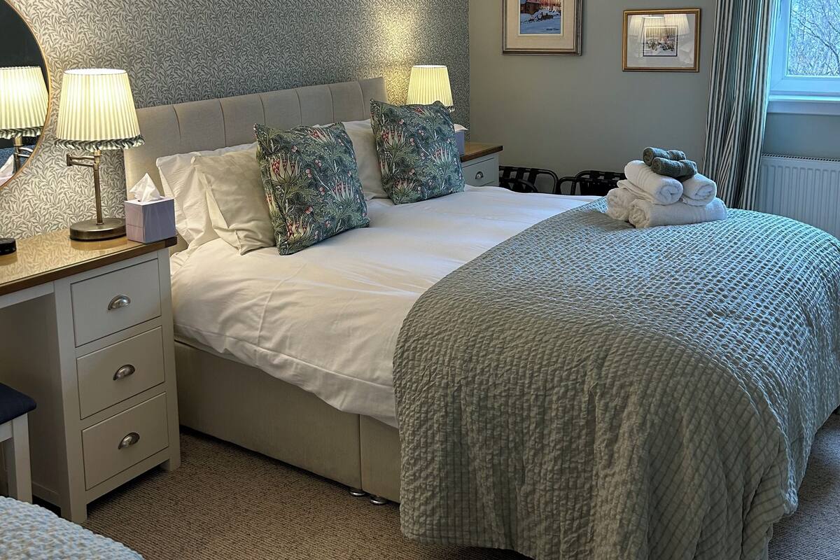 Quarto bem arrumado com cama, mesas de cabeceira e janela com cortinas.