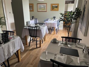 A dining area with multiple tables set for service, featuring white tablecloths and wooden chairs. - Castlecroft (Stirling)