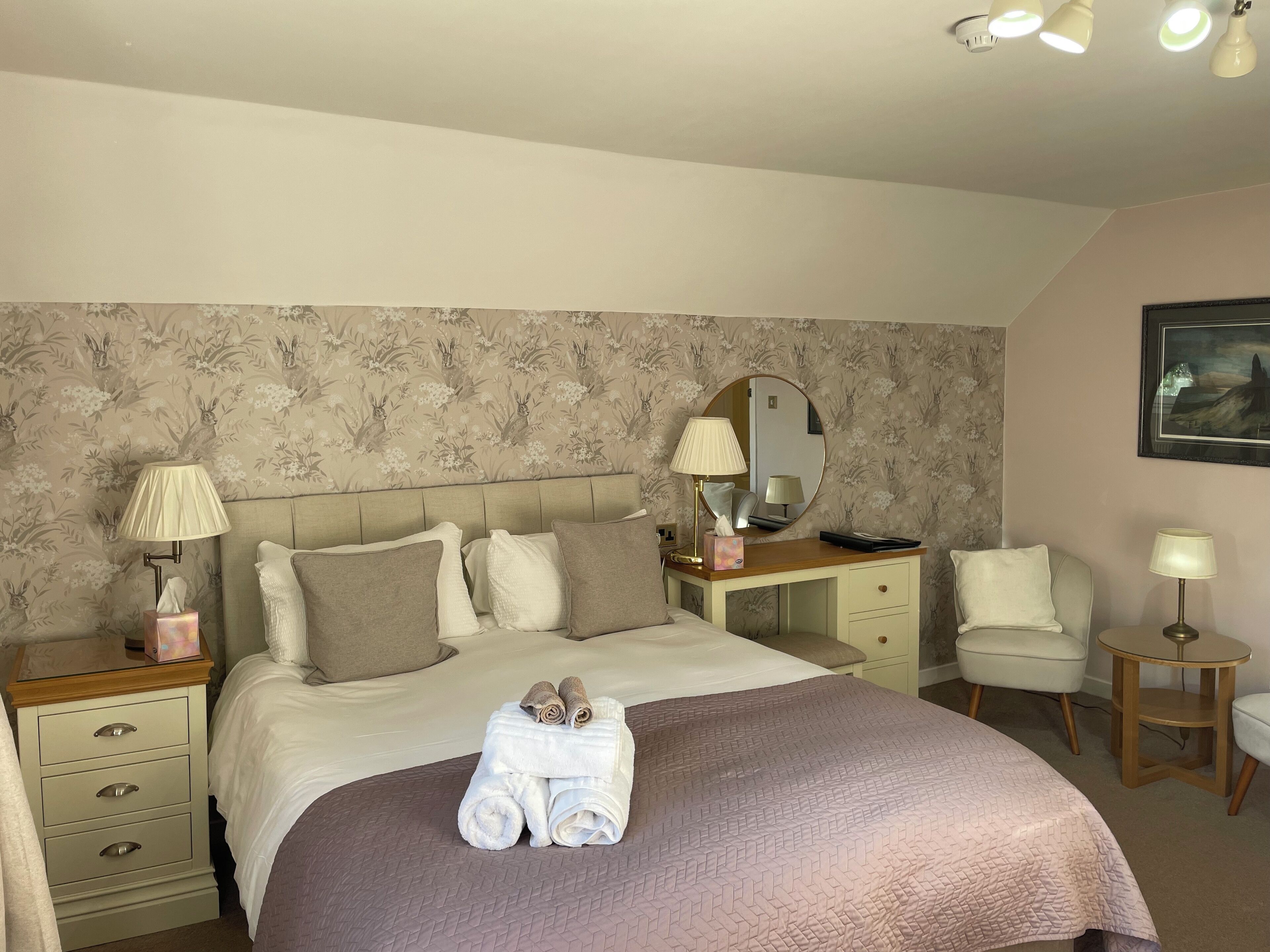 Un dormitorio ordenado con cama, mesitas de noche, una silla y un escritorio.