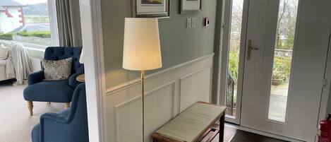 Une pièce avec un fauteuil bleu, un lampadaire, un banc et une porte donnant sur l’extérieur.