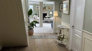 Un couloir avec un tapis à motifs, une porte blanche et une vue sur un salon doté d’une cheminée.