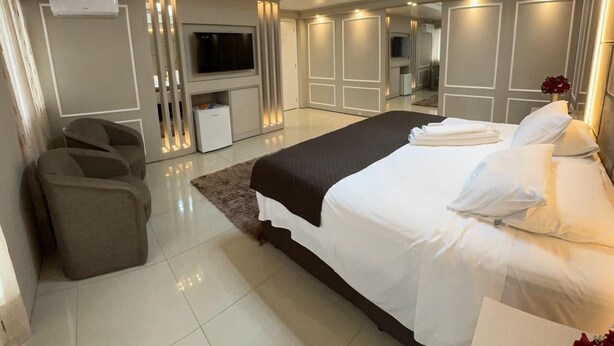 A modern bedroom with a large bed, a TV, and a seating area.