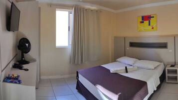Habitación de hotel con cama, escritorio, computadora, televisor y ventana con cortinas.