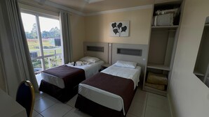 A hotel room with two beds, a window with curtains, a painting on the wall, and a wardrobe.