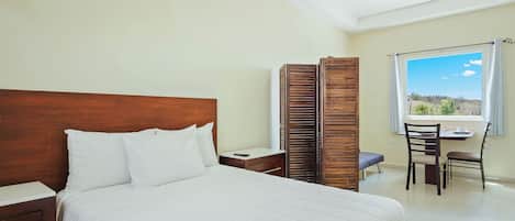 A bedroom with a wooden headboard, a bed with white bedding, a desk with a chair, and a window with a view.
