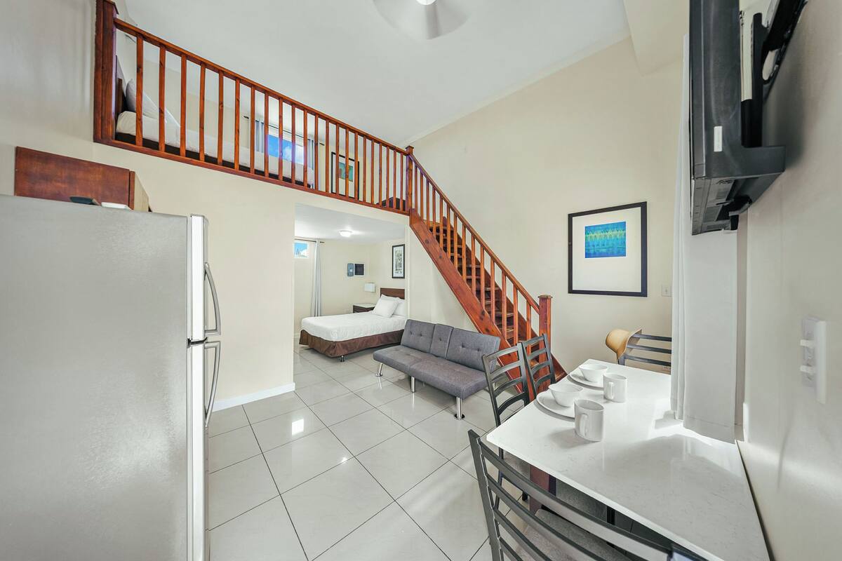 A compact hotel room with a kitchenette, a dining area, and a staircase leading to an upper level.
