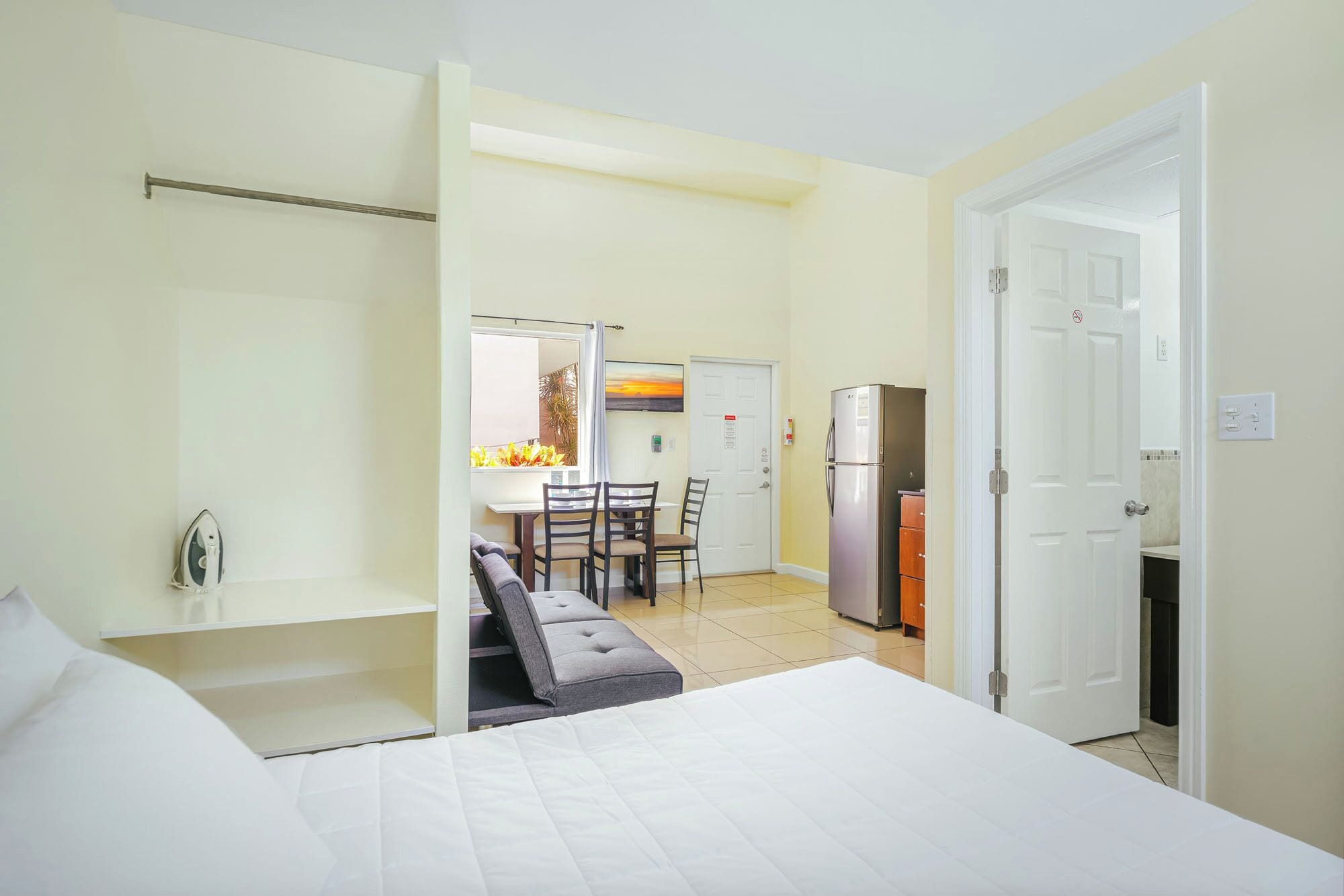 Une chambre d’hôtel comprenant un lit, un coin repas avec une table et des chaises, un réfrigérateur et une porte avec une pancarte.