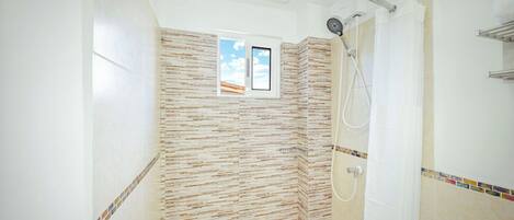 A shower with a curved glass door, a handheld showerhead, and a small window with a view of the sky.