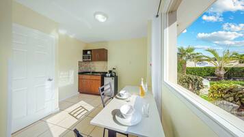 A compact kitchen with a dining area, a white door, and a view of a tropical garden through a window.