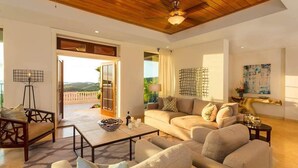 A spacious living room with a large sofa, a coffee table, and a view of the outdoors through a sliding glass door. - The Hills, St John (St. John)