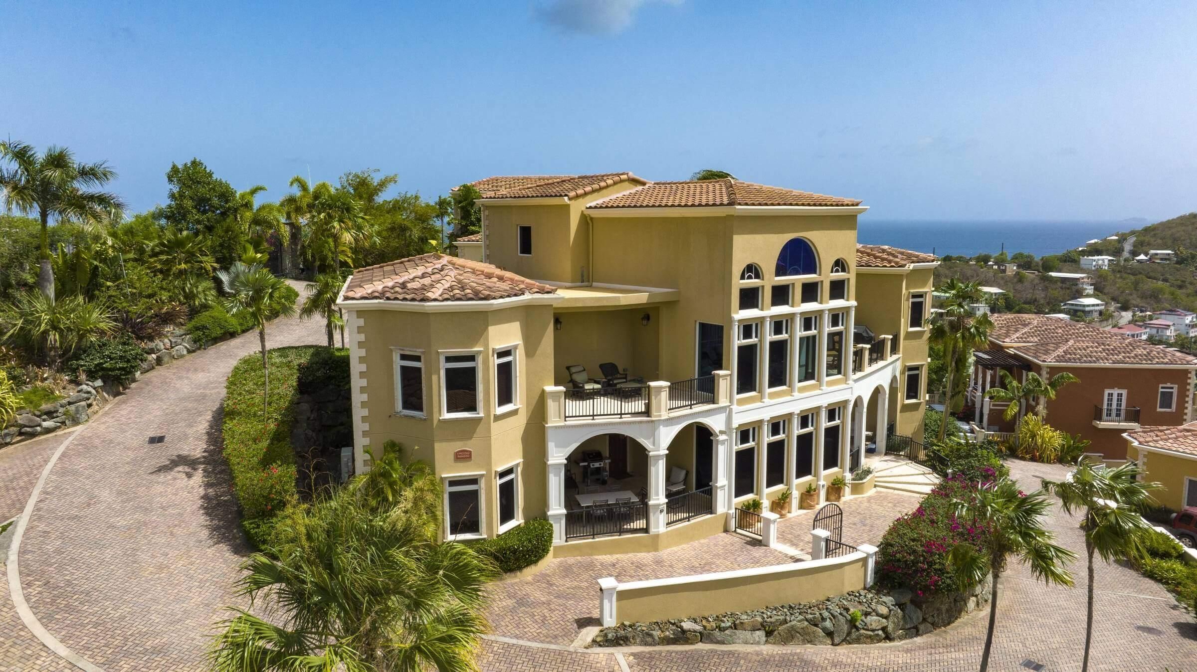 A large, two-story building with a balcony, surrounded by palm trees and a paved driveway.