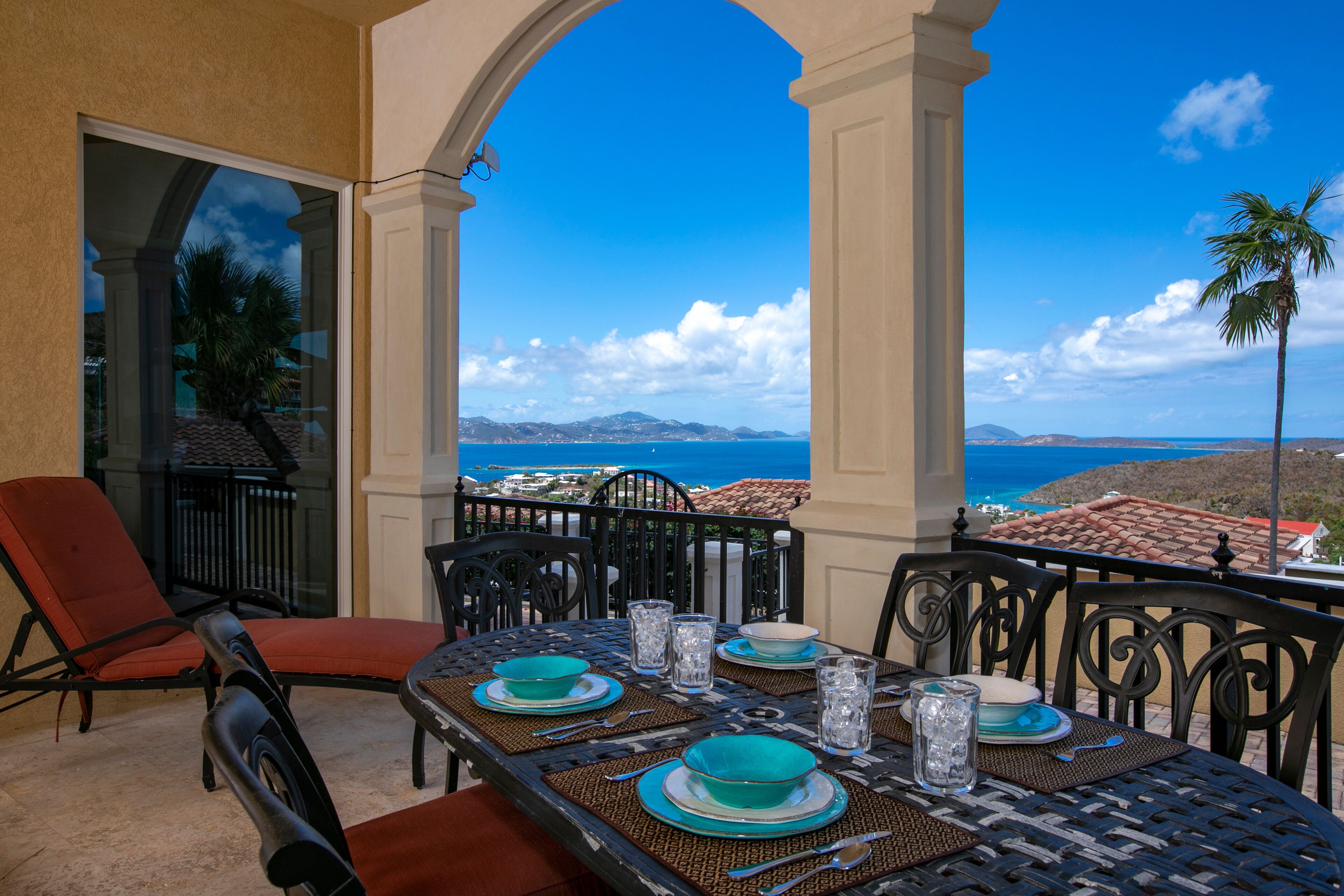 A dining area with a table set for four, overlooking a scenic view of the ocean and hills.