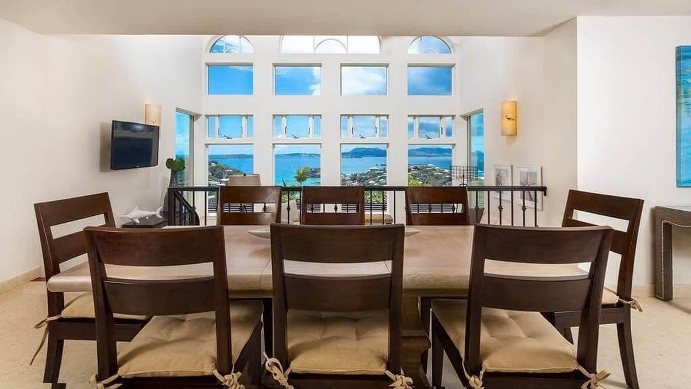 A dining area with a view of the sea, featuring a table with chairs and a TV mounted on the wall.