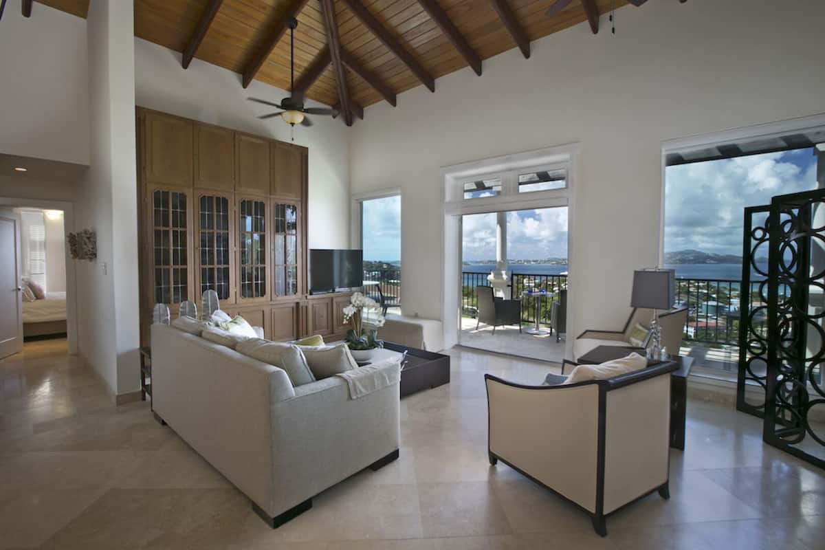 A spacious living area with a large sofa and armchair, a television, and a balcony with a view.