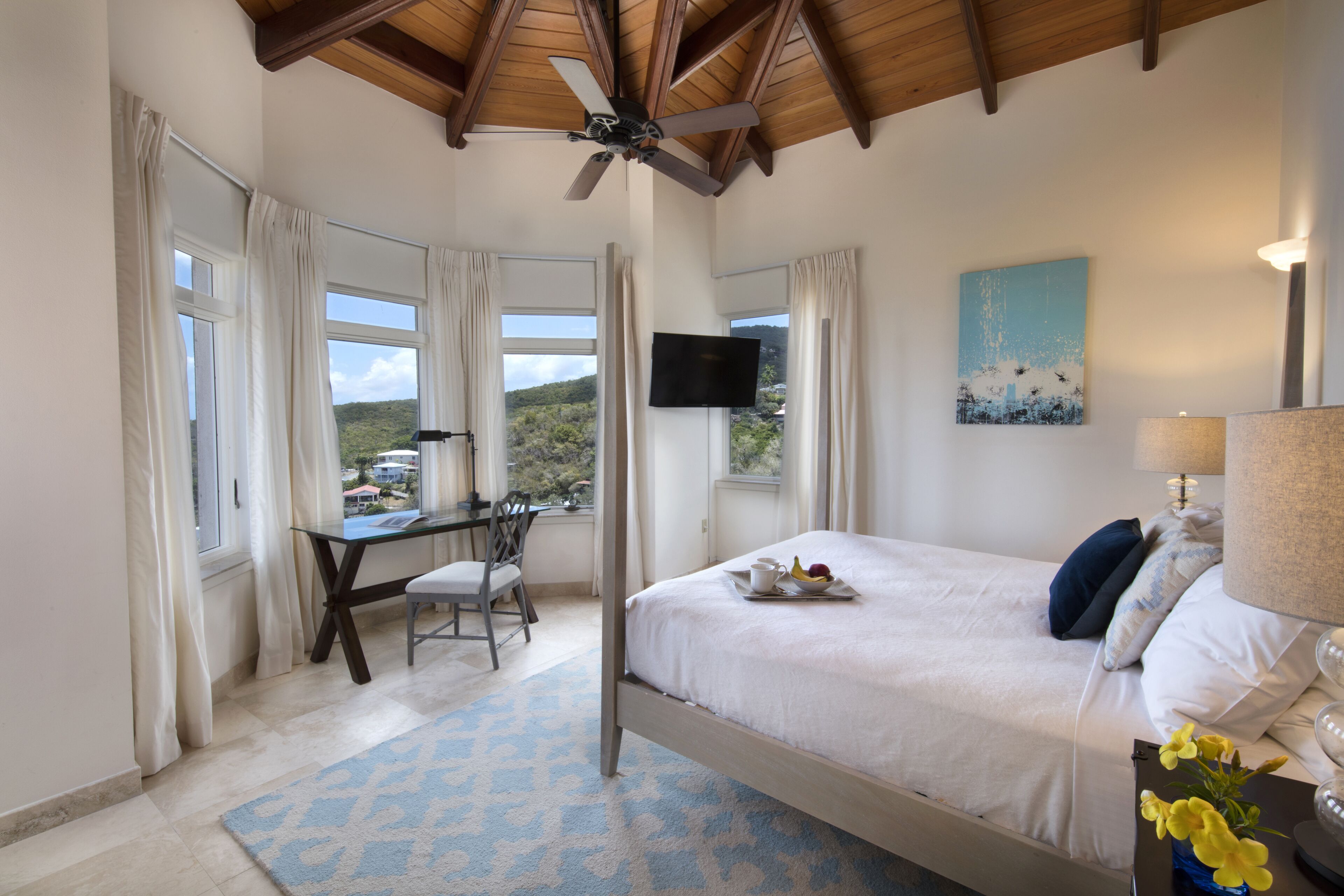 A bedroom with a bed, a desk, a chair, a TV, and a view of the outdoors.