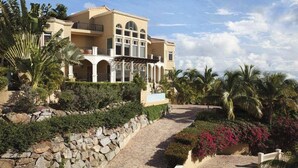 A large, multi-story building with a beige facade, arched windows, and a stone pathway leading to the entrance. - The Hills, St John (St. John)