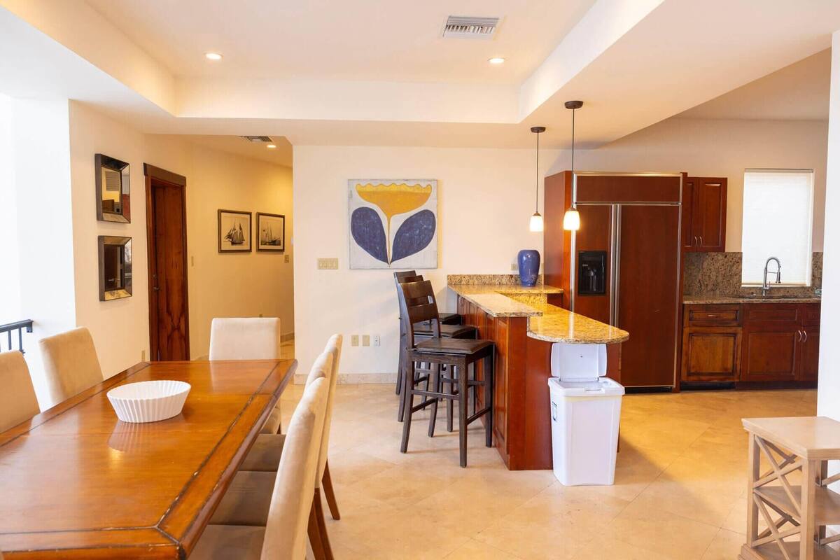 A modern kitchen with a central island, wooden cabinets, and a stainless steel refrigerator.