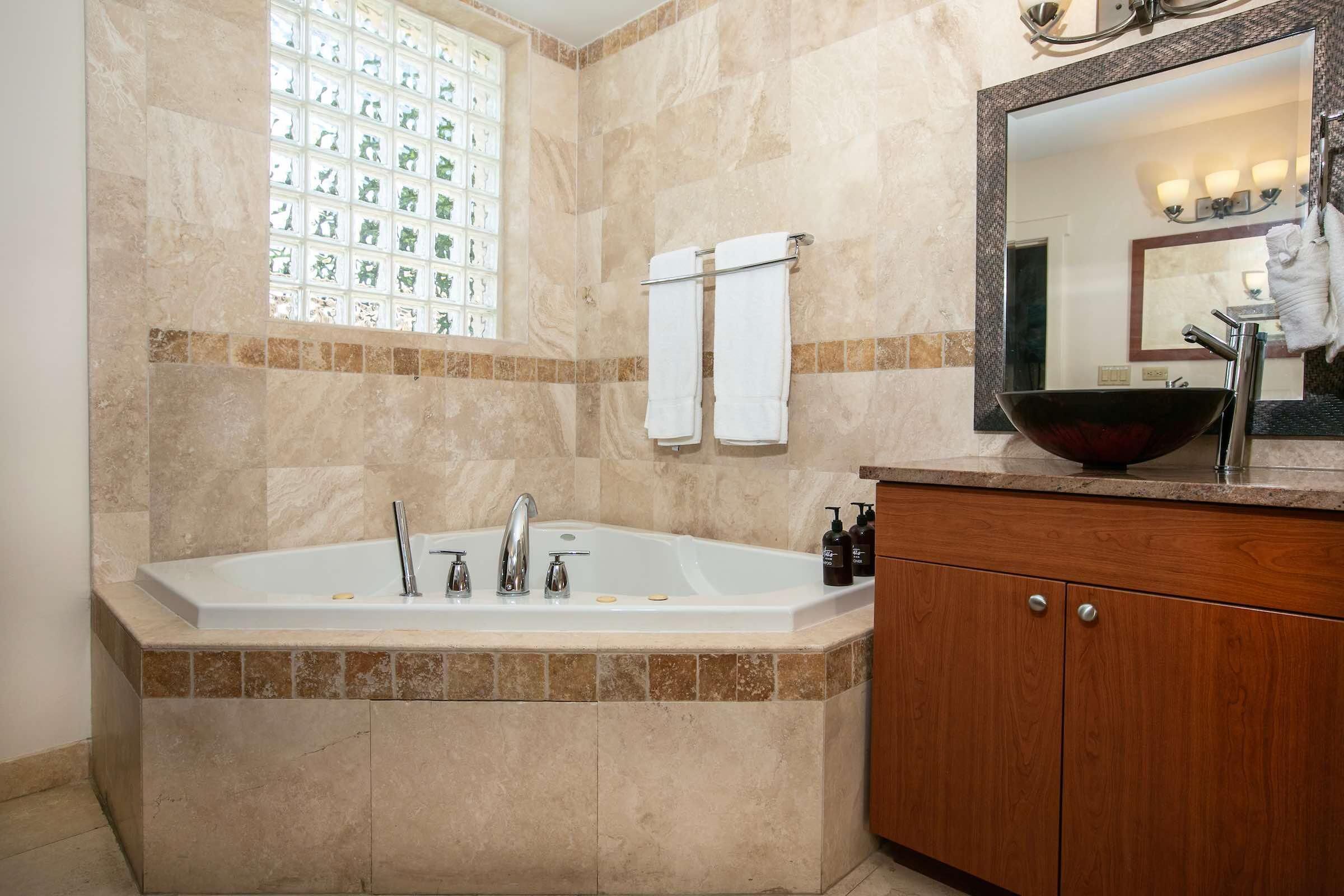 A bathroom with a large bathtub, a wooden vanity, a mirror, and a window with a decorative view.