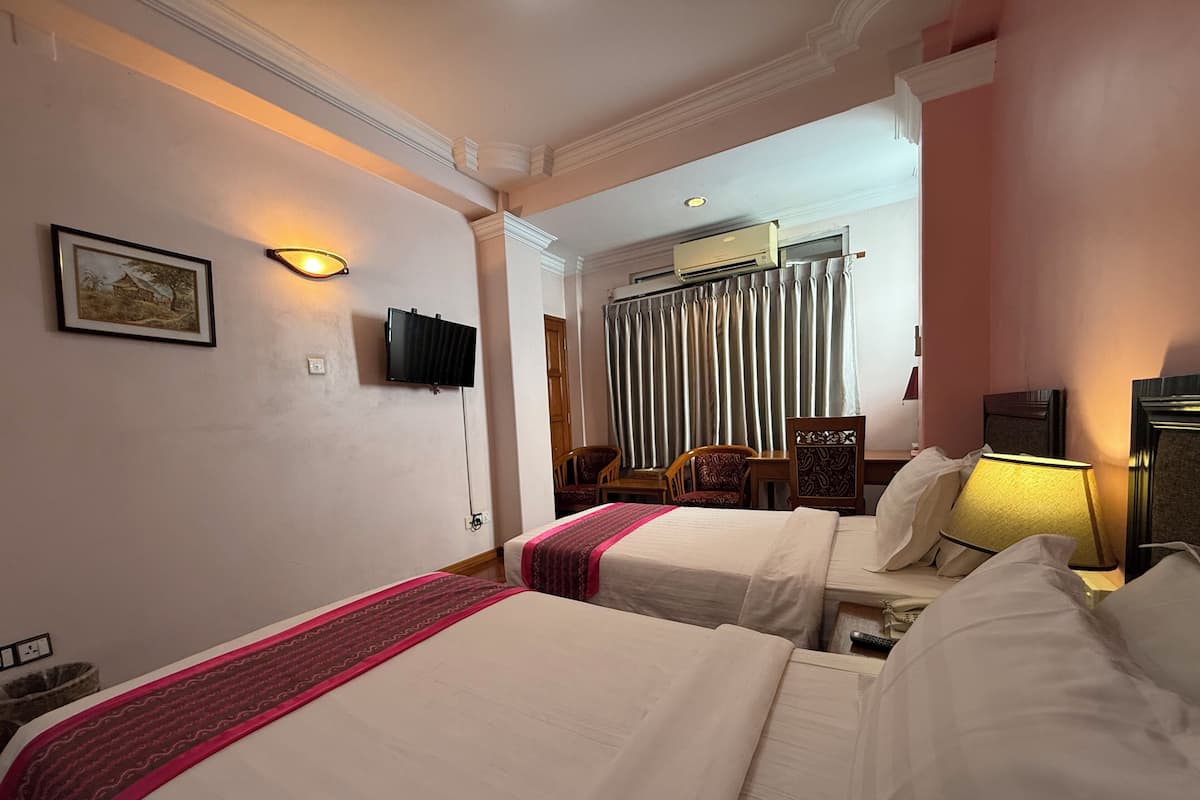 A hotel room with two beds, a television, a desk, a chair, a lamp, and a window with curtains.