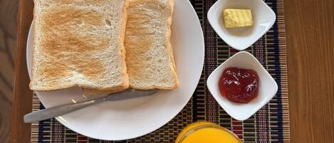 A breakfast tray with toast, fried eggs, butter, jam, and orange juice on a woven placemat.
