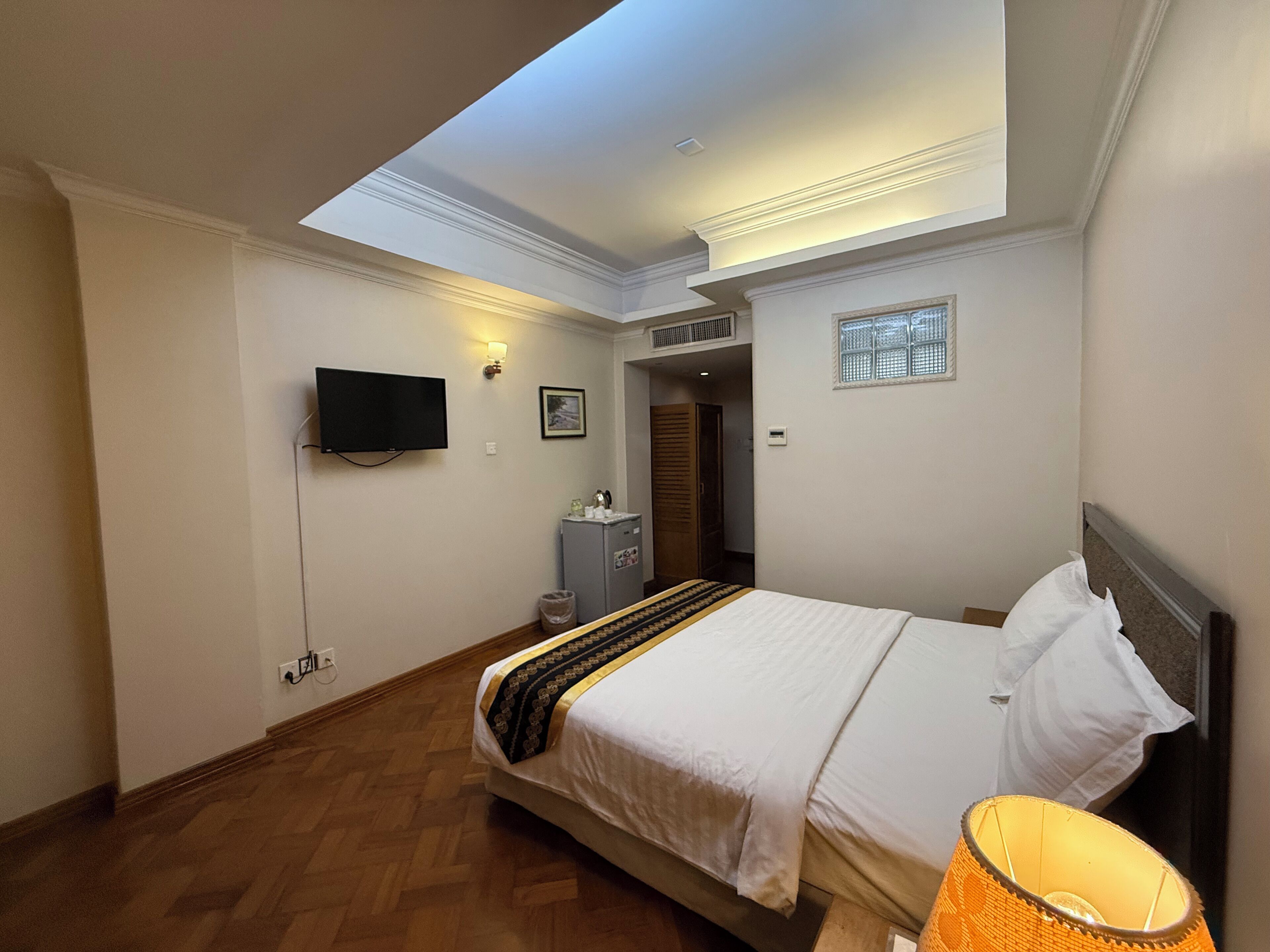 A bedroom with a bed, a television, a small cabinet, and a window.