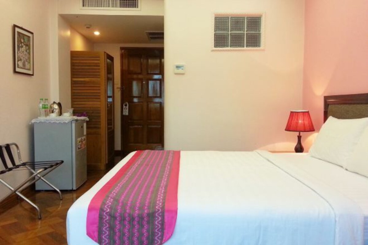 Habitación de hotel con una cama, un escritorio con una silla, un refrigerador y una puerta que da a otra habitación.
