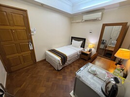 Habitación de hotel con cama, mesita de noche, lámpara y una pequeña mesa con hervidor y tetera.