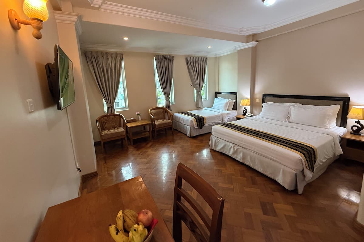 A hotel room with two beds, a dining table with fruit, and a TV.