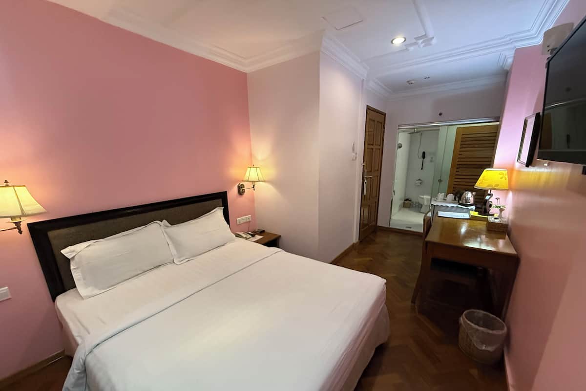A hotel room with a large bed, bedside lamps, a wooden dresser, and a mirror.